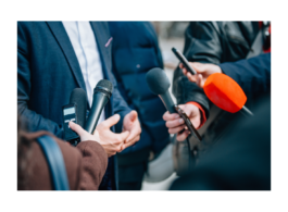 Imagem representa uma pessoa em frente a vários microfones dando entrevista para repórteres