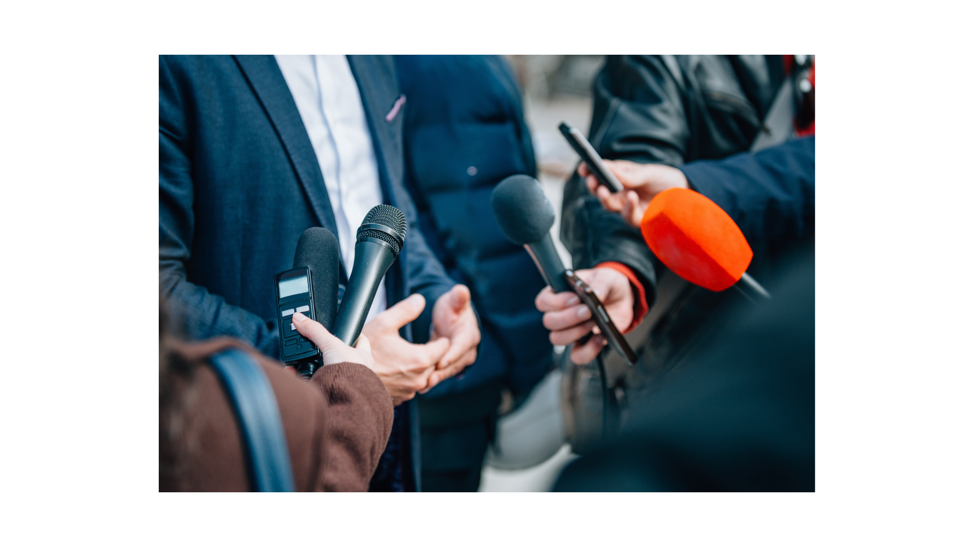 Imagem representa uma pessoa em frente a vários microfones dando entrevista para repórteres